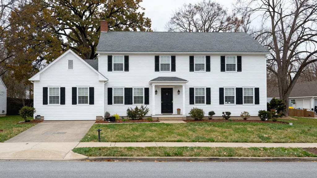 Two-story white colonial house with black shutters and a central portico beneath mature bare trees.