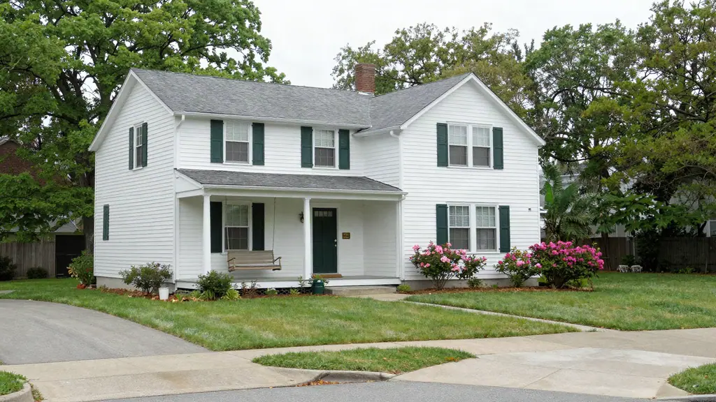 Two-story white house with a deep front porch, porch swing and blooming azaleas under a hazy sky.
